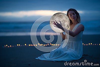Gentle image of a girl, Astrology, Female magic. Beautiful attractive girl on a night beach with sand hugs the moon, art Stock Photo