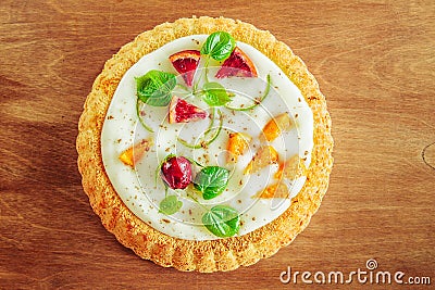 Gentle magnificent biscuit with vegetable vanilla cream decorated with fruit, a bud of a rose and young leaves on a wooden table, Stock Photo