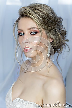 Gentle portrait of a beautiful cute happy bride with a beautiful hairdo festive bright make-up in a wedding dress with earrings an Stock Photo