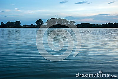 Gentle waves on the lake, trees on the horizon and clouds in the sky Stock Photo