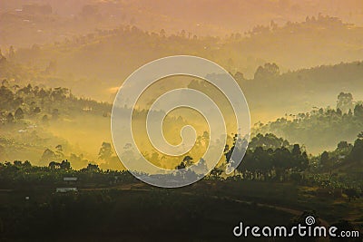 Gentle yellow light and light mist over the hills in country side with traditional houses and the tropical nature of Uganda Stock Photo