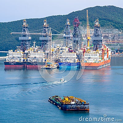 Tugboat sails pass driil ships in the Bay of Daewoo Shipbuilding and Marine Engineering DSME in Okpo city, South Korea. Editorial Stock Photo