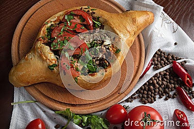 Georgian khachapuri with meat and tomatoes on a round kitchen board Stock Photo