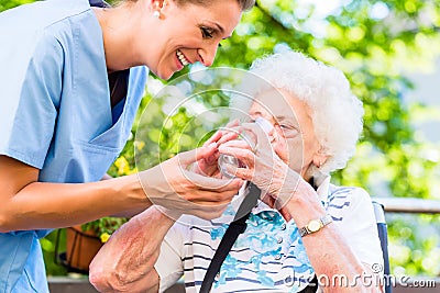 Geriatric nurse giving glass of water to senior woman Stock Photo