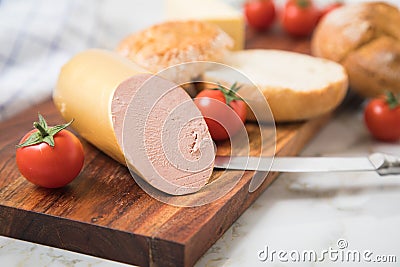 German fine veal liver sausage spread on crispy bread roll bun, with butter, tomatoes, wooden board, kitchen towel and light Stock Photo