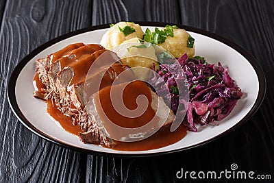 German food Sauerbraten - slowly stewed marinated beef with gravy with potato dumplings and red cabbage close-up on a plate. Stock Photo