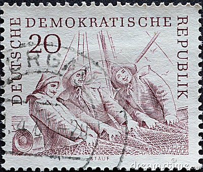 GERMANY, DDR - CIRCA 1961 : a postage stamp from Germany, GDR showing portrait of three fishermen in work clothes with hats haulin Editorial Stock Photo