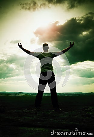 Gesture of triumph. Happy hiker in greyshirt and dark trousars. Tall man on the peak of sandstone cliff watching down to landscape Stock Photo