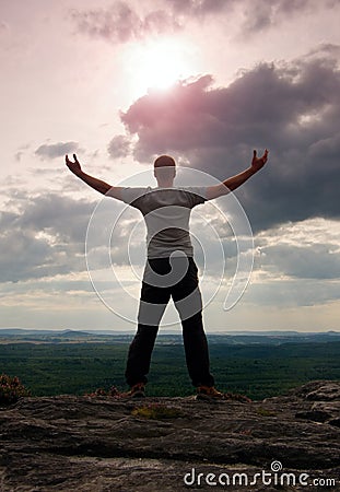 Gesture of triumph. Happy hiker in greyshirt and dark trousars. Tall man on the peak of sandstone cliff watching down to landscape Stock Photo