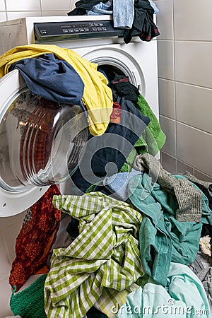 Giant pile of colorful dirty laundry and a washing machine stuffed full with clothes Stock Photo