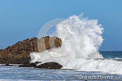 Giant wave breaking against large rock. Spray in the air; blue sky in the distance. Stock Photo