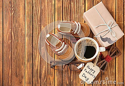 Gift box, cup of coffee, male accessories and baby shoes on wooden background. Happy Father\'s Day celebration Stock Photo