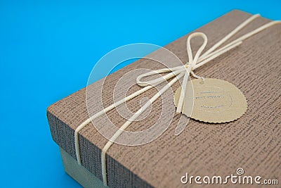 A gift box isolated over blue background with copy space. Box is tied with a cord with a label with Wishes and Happiness. Holiday Stock Photo