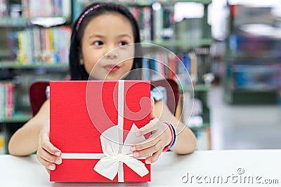 Gift box for kids girl. White box with red bow in the smiling asian girl hands for give a gift in the library, happy and surprise Stock Photo