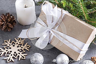 Gift box with white ribbon and rope, silver balls, spruce branch, candle, cone, snowflake, gray background Stock Photo