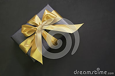 Gift box wrapped in black paper with gold ribbon on black surface. Stock Photo