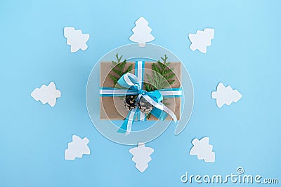 Gift box wrapped of craft paper, blue and white ribbons and decorated fir branches and pinecones on the blue background, top view. Stock Photo