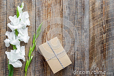 Gift box wrapped in craft paper near flower gladiolus on rustic wooden background top view copyspace Stock Photo