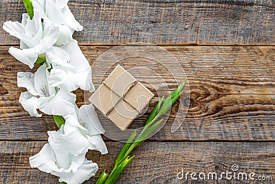 Gift box wrapped in craft paper near flower gladiolus on rustic wooden background top view copyspace Stock Photo