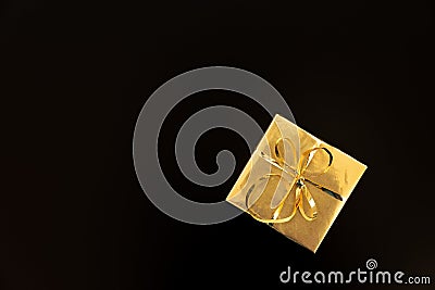 Gift box wrapped golden paper and ribbon on black background. Top view. Flat lay. Christmas and New Year holidays concept. Copy Stock Photo