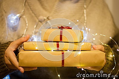 Gift boxes with red ribbon in the hands. Hands hold gifts in craft paper with luminous garland Stock Photo