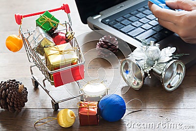 Gift boxes in shopping cart and Christmas decorations, Woman holding credit card on laptop computer Stock Photo