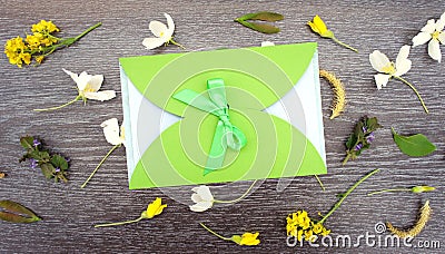 Gift envelope with green ribbon on floral wooden background. Congratulation with flowers. Flat lay Stock Photo