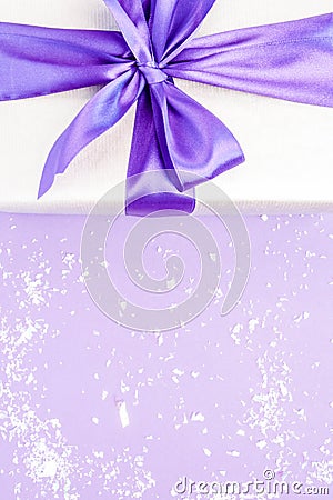 Gift with violet ribbon and bow-knot, snow on a violet background. Copy space Stock Photo