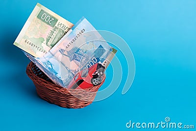 A gift in a wicker basket, money and a car in a hand-woven basket on a blue background Stock Photo