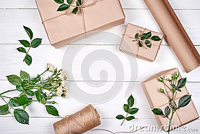 Gift wrapping background. Rolls of kraft wrapping paper, twine, branch of roses, gift boxes on wooden background, copy space. Stock Photo