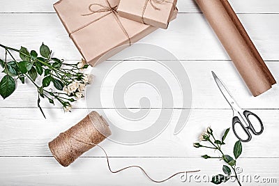 Gift wrapping background. Rolls of kraft wrapping paper, rope, branch of roses, gift boxes and scissors on wooden background Stock Photo