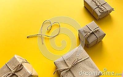 Gift wrapping in kraft paper with a heart made of threads on a yellow background. Minimalism. The concept of the holiday, love, bi Stock Photo
