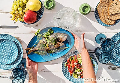 Gilt-head bream also known as Orata grilled on a barbeque grill served by a woman on a white wooden table with vegetable salad and Stock Photo