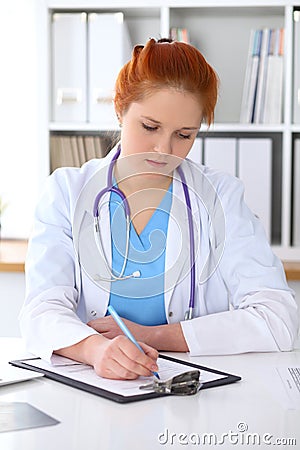 Ginger female doctor filling up medical form on clipboard closeup. Healthcare, insurance and medicine concept Stock Photo