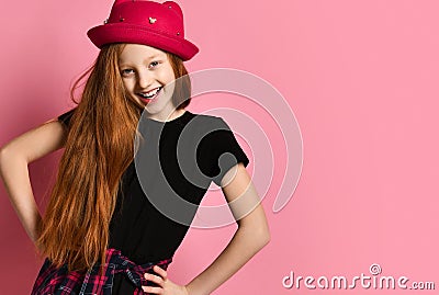 Teen female in black dress, checkered shirt on waist, red hat. She is laughing, hands on hips, posing on pink background. Close up Stock Photo
