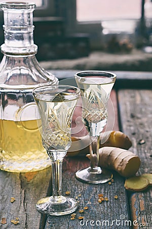 Ginger tincture or ale on wooden background. Spice yellow liqueur in a glass. Homemade Alcohol drink. Rustic style. Stock Photo