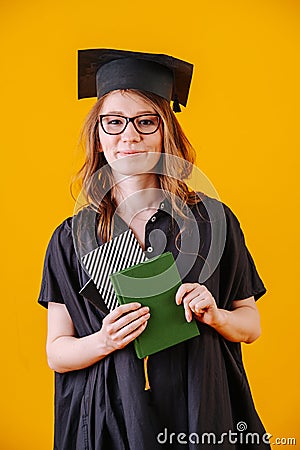 Girl in academic dress with diploma in her hands on a yellow background Stock Photo