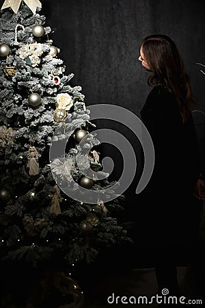 A girl admires a decorated New Year tree at home in the evening Stock Photo