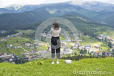 Girl admires the village in the valley. Mountains in the distance. Back view Stock Photo