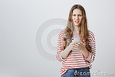 Girl is annoyed with spam on her mailbox. Portrait of bothered and confused caucasian woman holding smartphone, looking Stock Photo