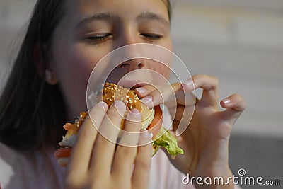 Girl with appetite eats delicious hamburger. child bites off large piece of sandwich Stock Photo