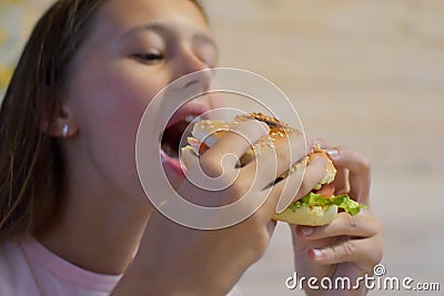 Girl with appetite eats delicious hamburger. child bites off large piece of sandwich Stock Photo