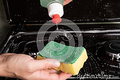 Girl applies detergent to a yellow washcloth close-up, cleaning the surface on the gas stove Stock Photo