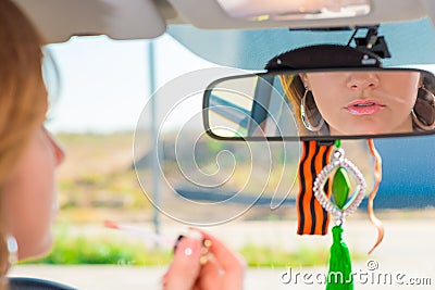 Girl applies lipstick behind the wheel of the car Stock Photo
