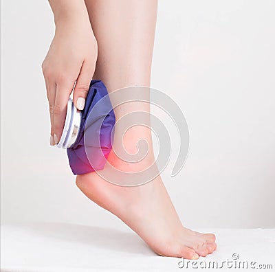 The girl applies a medical ice bag to the ankle joint to eliminate pain and relieve swelling. Cold joint treatment Stock Photo