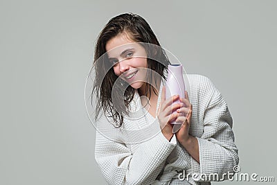 Girl applying hair conditioner. Young brunette woman with nourished long hair, studio shot. Woman hold bottle shampoo Stock Photo