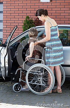 Girl assisting disabled woman getting into a car Stock Photo