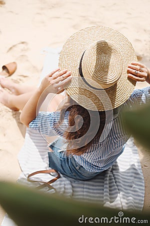 The girl from the back in the hat sits on the sand Stock Photo