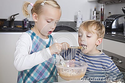 Girl baking cookie while brother tasting batter in kitchen Stock Photo