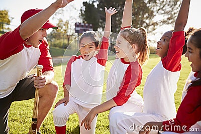 Girl baseball team kneeling with their coach, raising hands Stock Photo